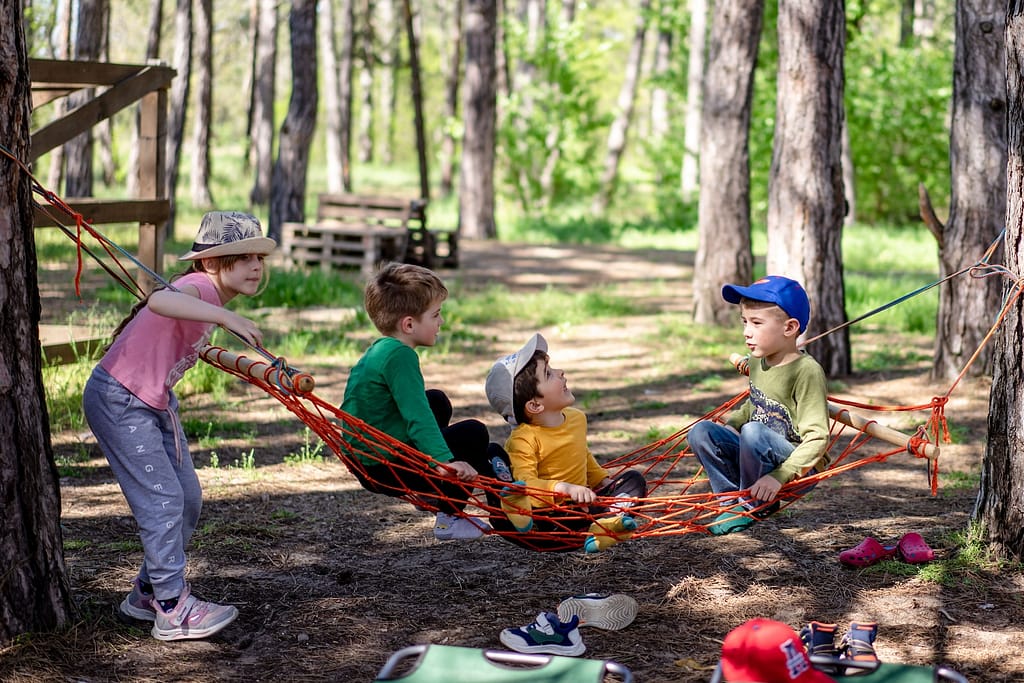 a group of kids sitting in a hammock in the woods